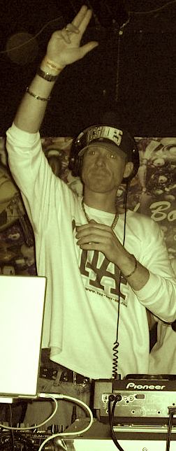 DJ Natural Nate® in sepia tone at Pioneer mixer in TLA long sleeve, hand raised holding mic